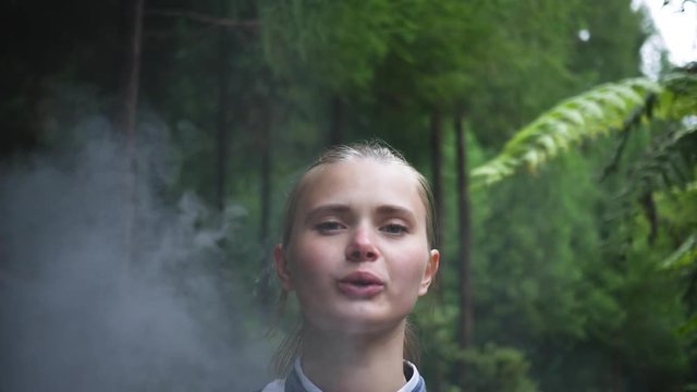 girl uses vape in the forest blows smoke close-up