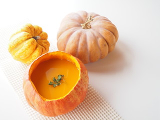 Homemade pumpkin soup served in a pumpkin bowl with other squash varieties, white background