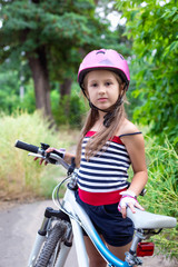 Little cute girl in a pink helmet near a bicycle