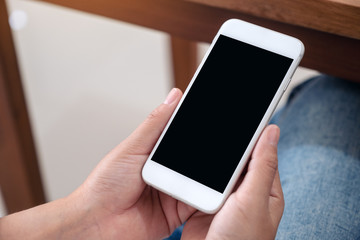 Mockup image of a woman holding black mobile phone with blank desktop screen while sitting
