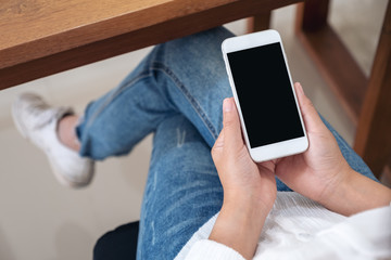 Mockup image of a woman holding black mobile phone with blank desktop screen while sitting