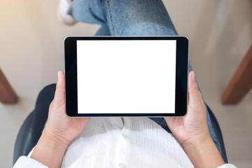 Top view mockup image of a woman holding black tablet pc with blank white screen horizontally while sitting on a chair