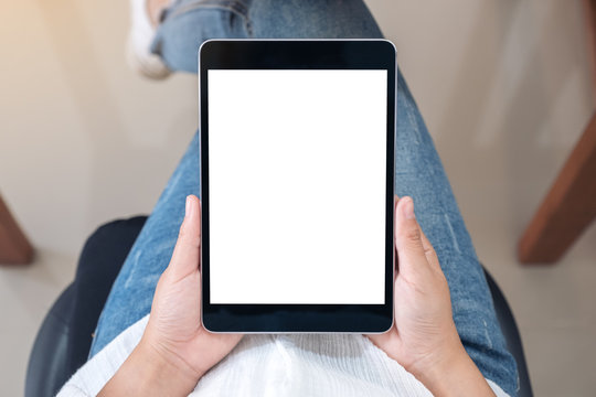 Top view mockup image of a woman holding black tablet pc with blank white screen while sitting on a chair