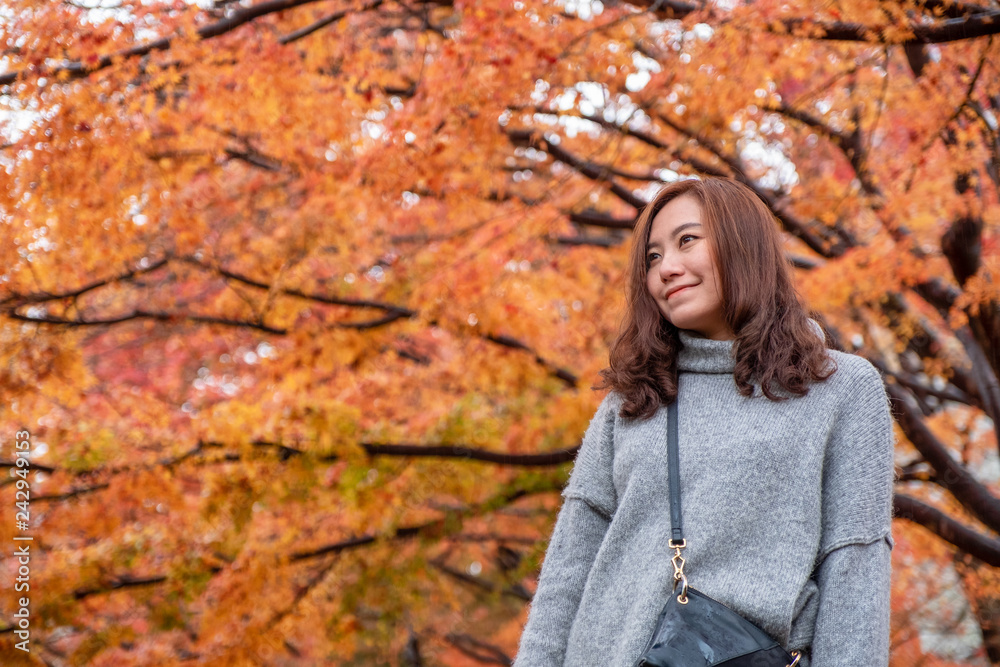 Wall mural a beautiful asian woman enjoyed standing in the garden with red and orange tree leaves in autumn bac