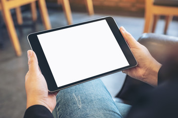 Mockup image of a woman holding black tablet pc with blank white screen horizontally while sitting in cafe