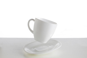 White cup with saucer in a jump on a white background. Jumping cup. Flying dishes on a white background.White dishes on a white background