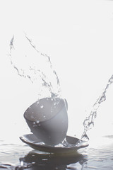 White cup and saucer with splashes of water.Vertical photograph of glass and water on a white background.
