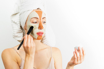 Beauty procedures skin care concept. Young woman applying facial gray and red mud clay mask to her face in bathroom. Woman with different masks on her face multi-masking 