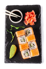The concept of Japanese cuisine. Rolls with salmon, feta cheese, cucumber. Near soy sauce, ginger and wasabi. Modern serving dishes in the restaurant on a black slate blackboard. On a white background