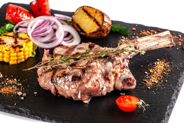 Large meat steak on the bone, grilled, served with grilled vegetables, corn, red onion, sweet...