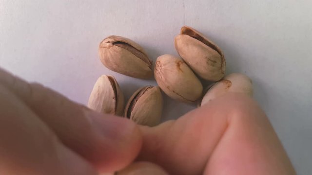 closeup of hands opening a pistachio - background with many pistachios