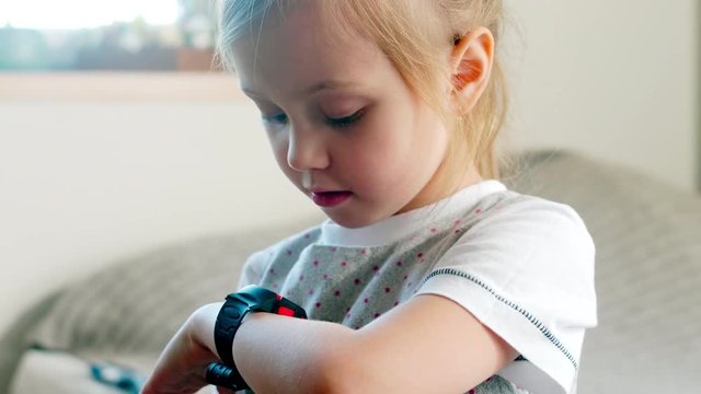 Close-up of cute little girl using smartwatch with voice command and listening to display while learning new gadget at home