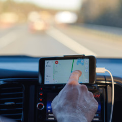 European man is searching appropriate route while driving a car, he is using his smartphone.