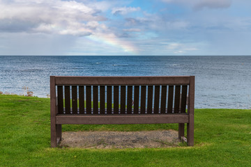 Fototapeta na wymiar A bench with a Rainbow over the North Sea coast, seen in Benthall, Northumberland, England, UK