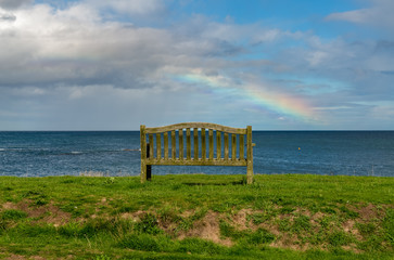 A bench with a Rainbow over the North Sea coast, seen in Benthall, Northumberland, England, UK