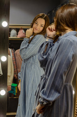 lifestyle fashion portrait of young stylish hipster woman in womens store showroom, standing near clothes rack indoors. Stylish wardrobe, wearing cute trendy outfit