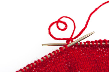 Red wool and knitting needles with a heart shape symbol on white background with copy space for text