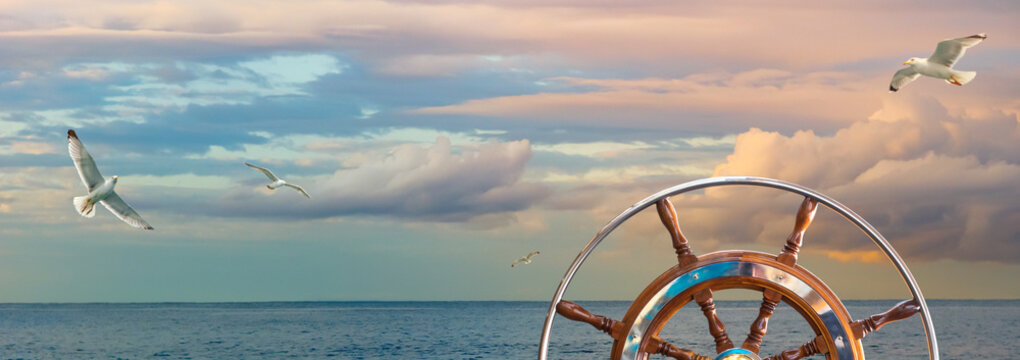 Marine sunrise with cloudy sky in pastel colors and flying seagulls over the ocean. Calm seascape with a skippers wheel on a ship for your concept of sea voyage or nautical expedition.