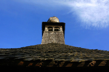 Fototapeta na wymiar Old wooden church roof with bell tower profile on blue sky.