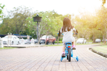 Asian child or kid girl enjoy happy with fun cycling on blue bike or bicycle on the public park with green garden and tree for sport exercise with healthy on summer or winter relax holiday on sunlight