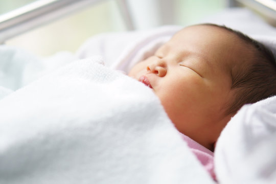 asian newborn baby or head and face infant sleep in white towel with diaper and innocent on bed and have lymph node on nose in children hospital