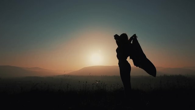 Silhouette of a beautiful young woman running in the mountains with a pareo in her hands. Slow motion. The concept of freedom, ease, success, rest. Sunset