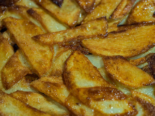 Golden slices of fried potatoes in vegetable oil in a frying pan.