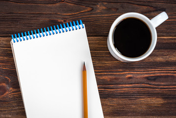 Notepad with yellow pencil and coffee on wooden background. Goals for the new year. Planning and schedule concept. To do list.