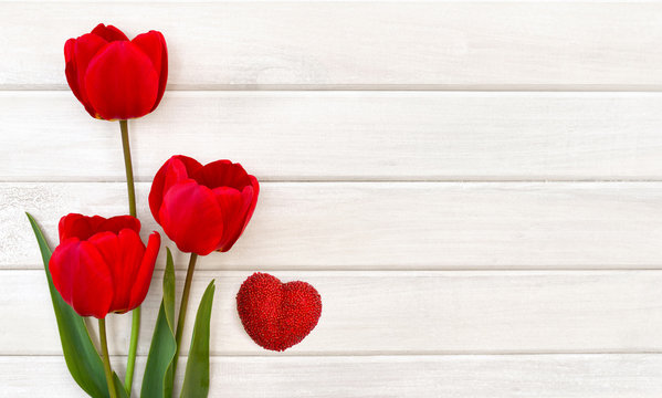 Decoration of Valentine Day. Beautiful red tulips and red heart on background of white painted wooden planks with space for text. Top view, flat lay - Powered by Adobe