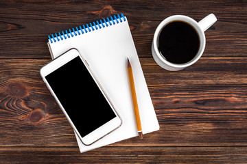 Notepad with yellow pencil, coffee and mobile phone on wooden background. Goals for the new year. Planning and schedule concept. To do list.