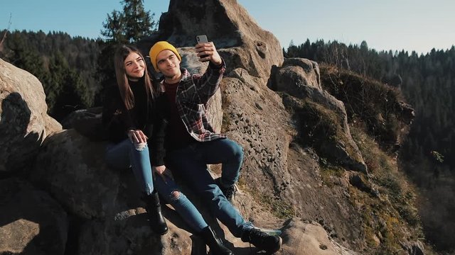 Young couple in love sits on the rock and take a selfie portrait. Man and woman visiting famous tourist attraction
