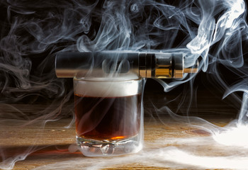 Electronic cigarette on a glass of whiskey in a cloud of vapor