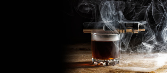 Electronic cigarette lying on a glass of brandy shrouded in steam