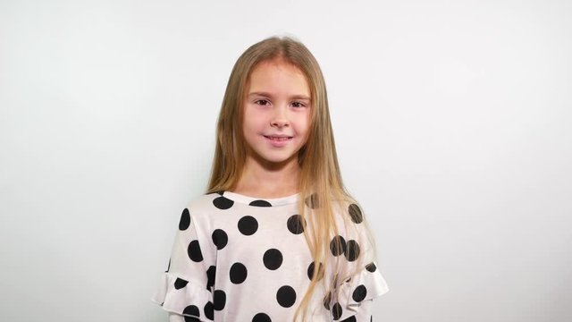 Smiling young girl in white top with black dots sends air kiss at the camera