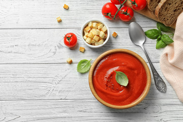 Fresh homemade tomato soup served with bread and croutons on white wooden table, top view. Space for text