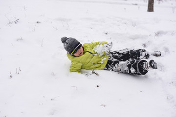 Boy falls down on snow. Winter fun. Child is rolling in the snow