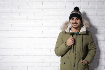 Young man wearing warm clothes against brick wall, space for text. Ready for winter vacation