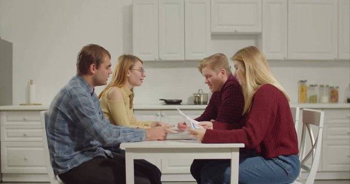 Group of college students gathered at table to discuss important issues of new university project in domestic room. Teenagers brainstorming, sharing ideas, taking active part in educational process.