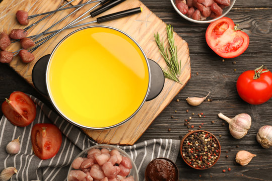 Flat lay composition with oil pot and meat fondue ingredients on wooden background
