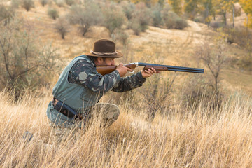 Fototapeta premium Hunter with a hat and a gun in search of prey in the steppe 