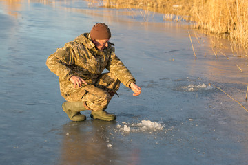 Naklejka premium The guy on the winter fishing at the hole catches a small fishing pole. Fishing on the lake with reeds on a beautiful winter day.
