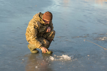 Naklejka premium The guy on the winter fishing at the hole catches a small fishing pole. Fishing on the lake with reeds on a beautiful winter day.