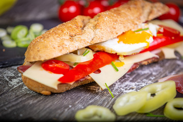 Fresh baguette sandwiches with bacon, cheese, tomatoes on wooden background