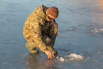 Fototapeta premium The guy on the winter fishing at the hole catches a small fishing pole. Fishing on the lake with reeds on a beautiful winter day.