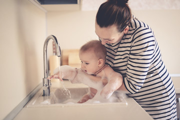 Mom takes care of baby, bathes baby sink with foam