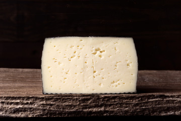 block of spanish sheep cheese on wooden board on dark background