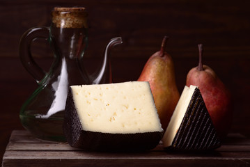 block of sheep cheese and whole fruits on rustic wooden board