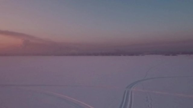 Flying over snow field sunset and lonely chimney-stalk with smoke on the horizon