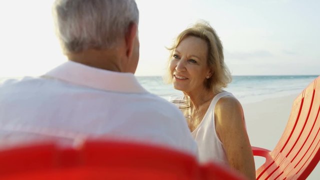 Retired Caucasian couple relaxed together on beach chairs sunset