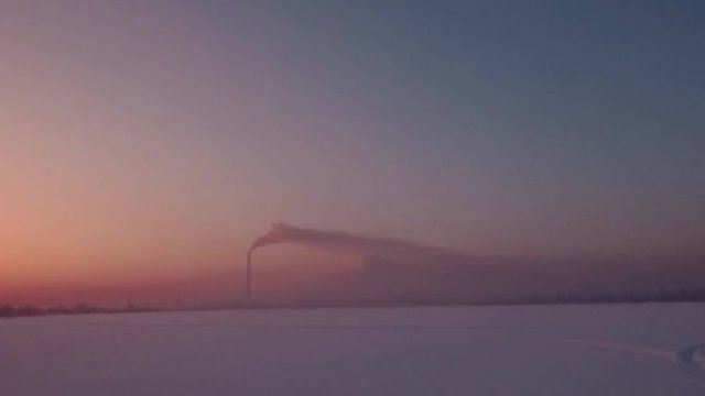 Flying over snow field sunset and lonely chimney-stalk with smoke on the horizon